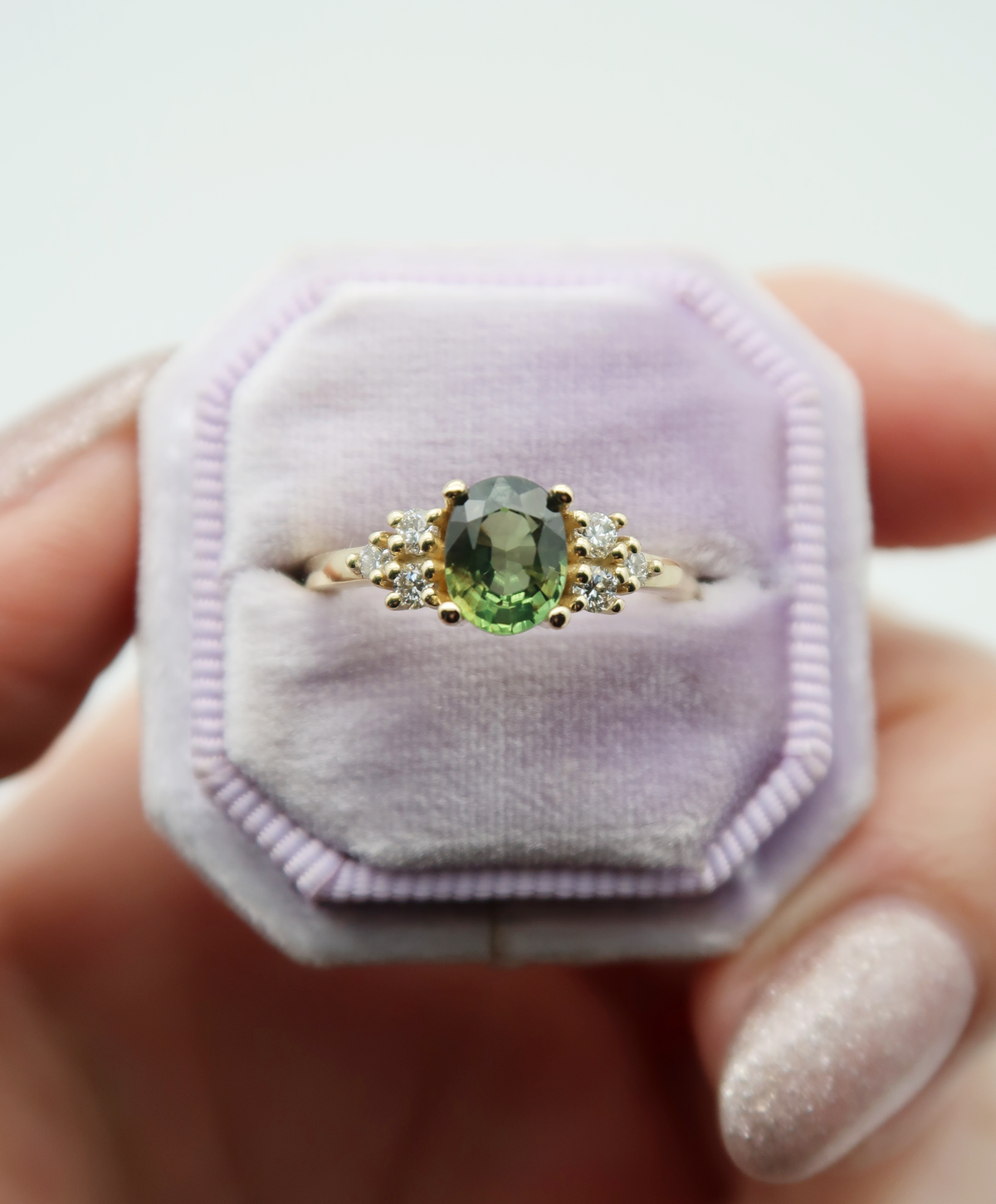 14K yellow gold custom engagement ring featuring a stunning golden green oval cut sapphire flanked by two clusters of sparking diamonds.