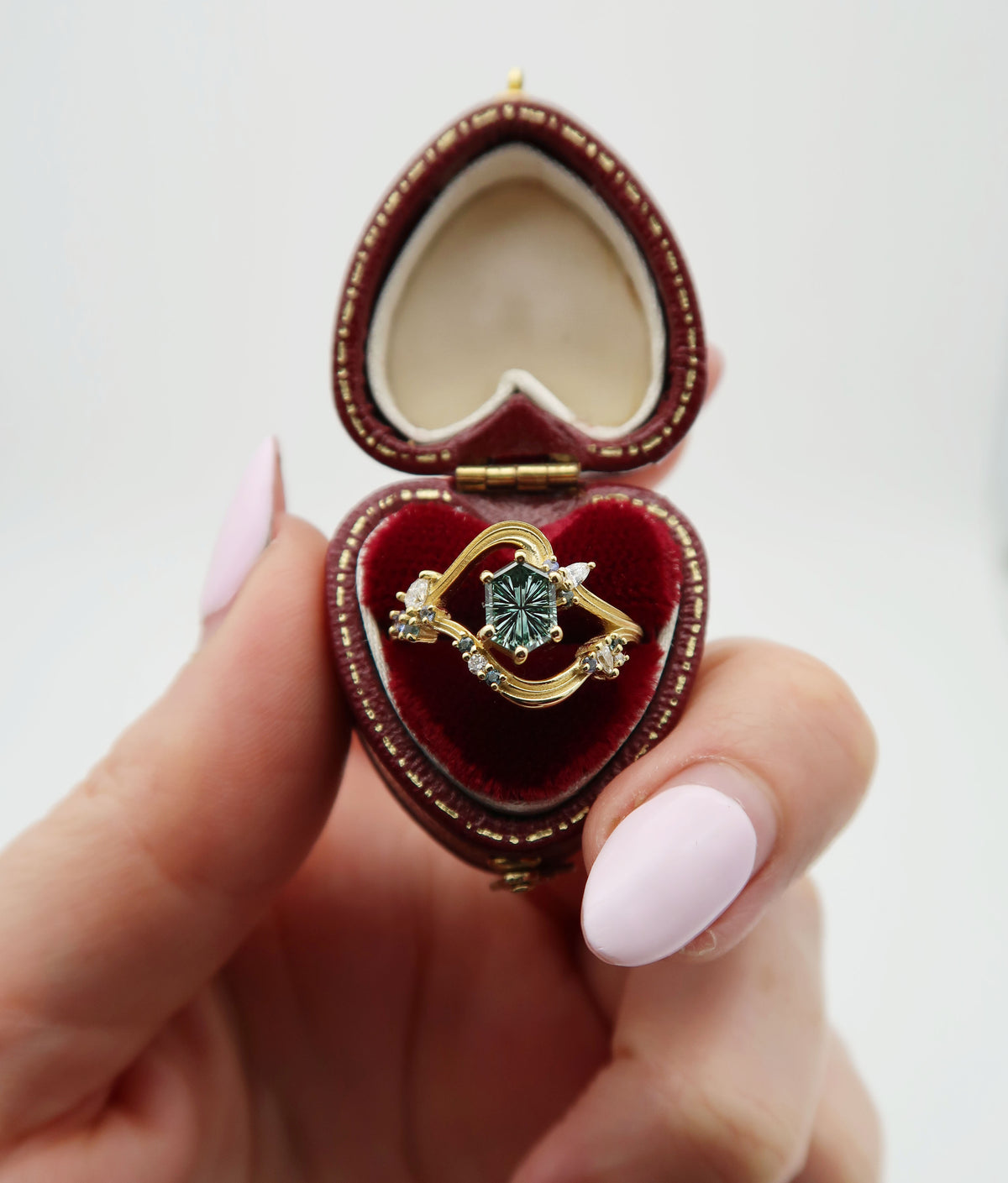 18k yellow gold and a one-of-a-kind John Dyer fantasy-cut sapphire engagement ring featuring a textured and sculptural wave design and teal and blue accent stones. Inspired by the colour of the groom-to-be’s eyes and the couple’s mutual love of the ocean. 