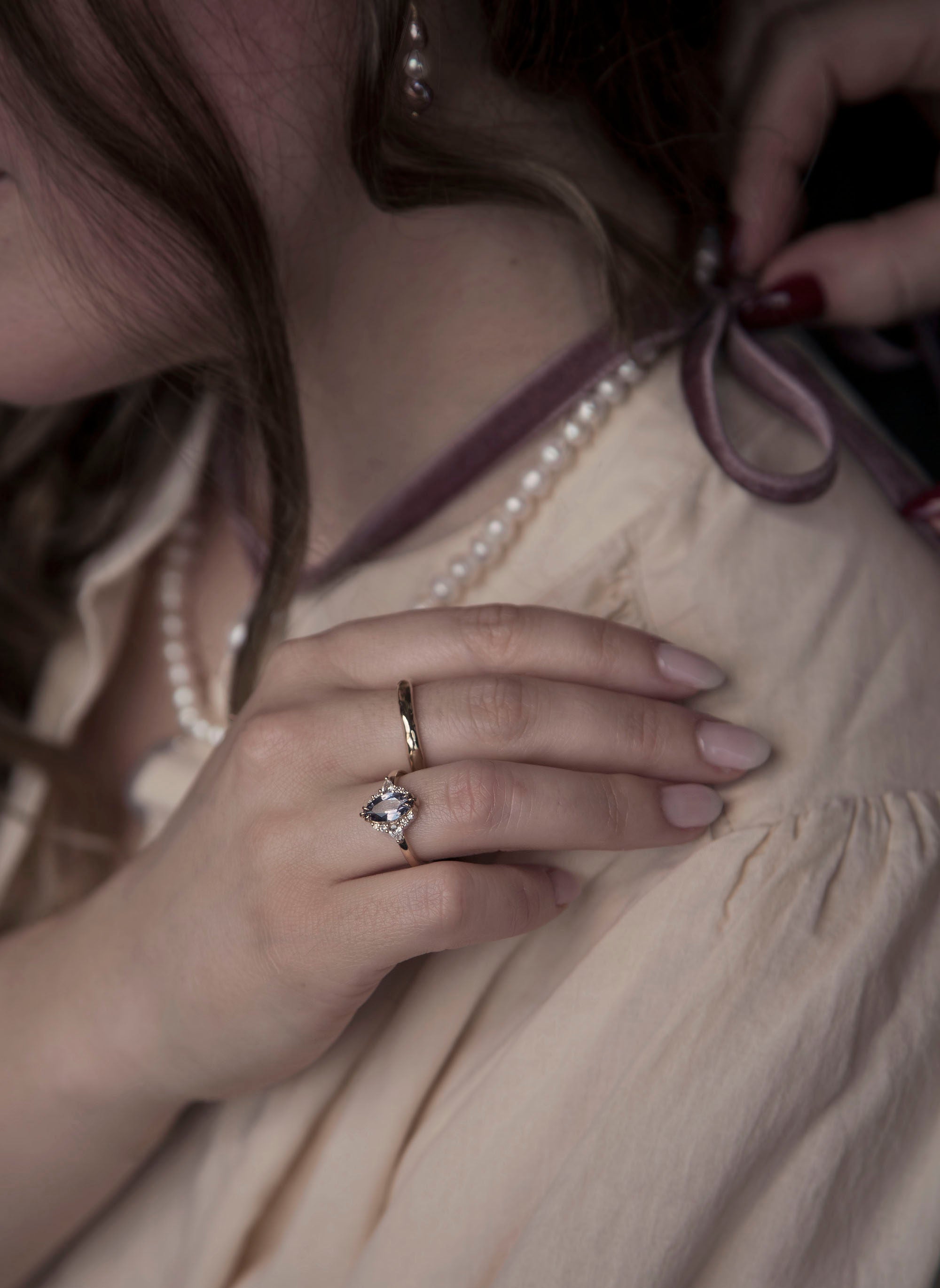 Woman in a beige linen dress, while wearing a handcrafted gold wedding band and a bespoke diamond engagement ring each designed by Invidiosa Jewellery.
