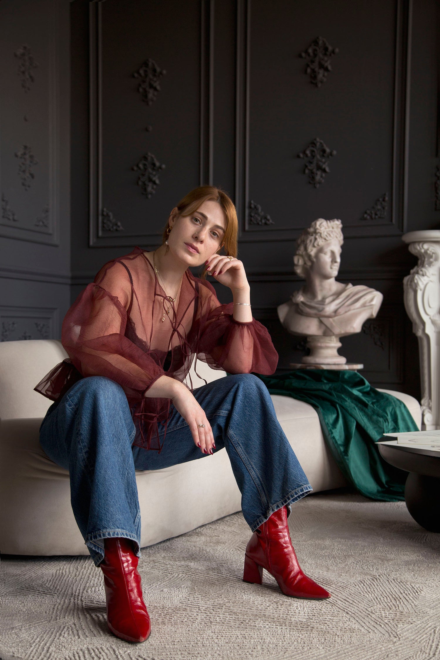 Portrait of the founder of Invidiosa Jewelry, Tessa, while wearing red boots, jeans, and a sheer red top all accompanied by bespoke earrings, necklaces, and rings that she handcrafted in her Toronto studio.