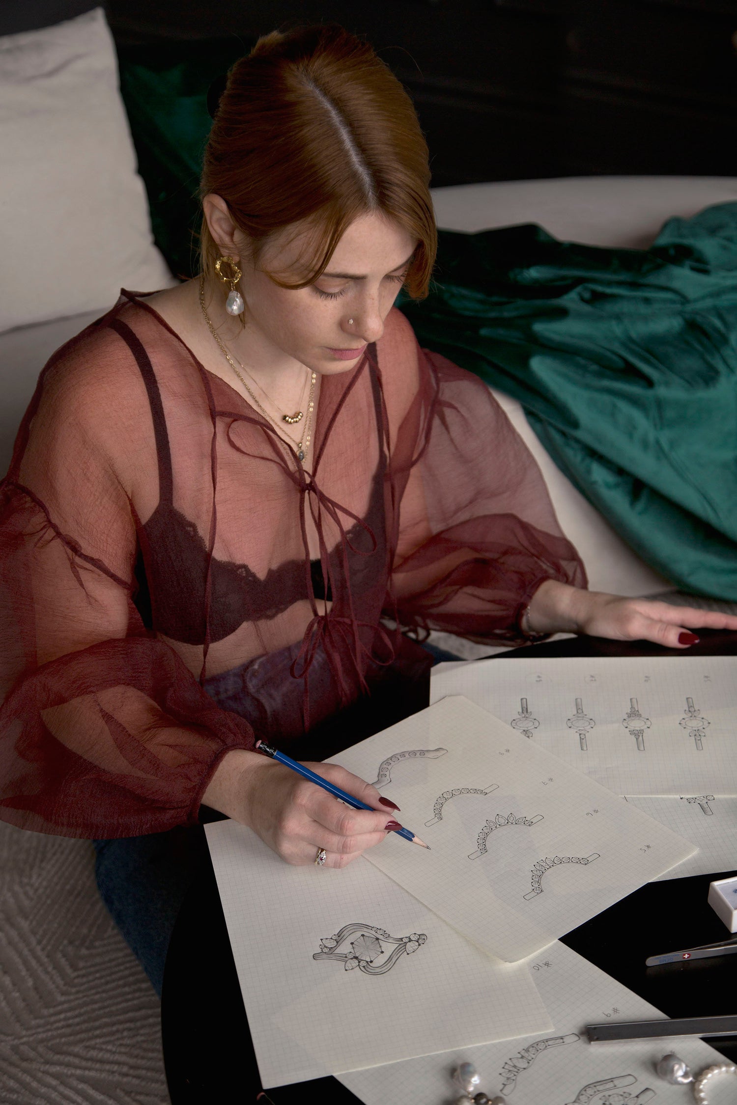 Founder of Invidiosa Jewellery, sketching custom jewellery designs while wearing bespoke rings, necklaces, and earrings that she handcrafted and designed in her Toronto studio 