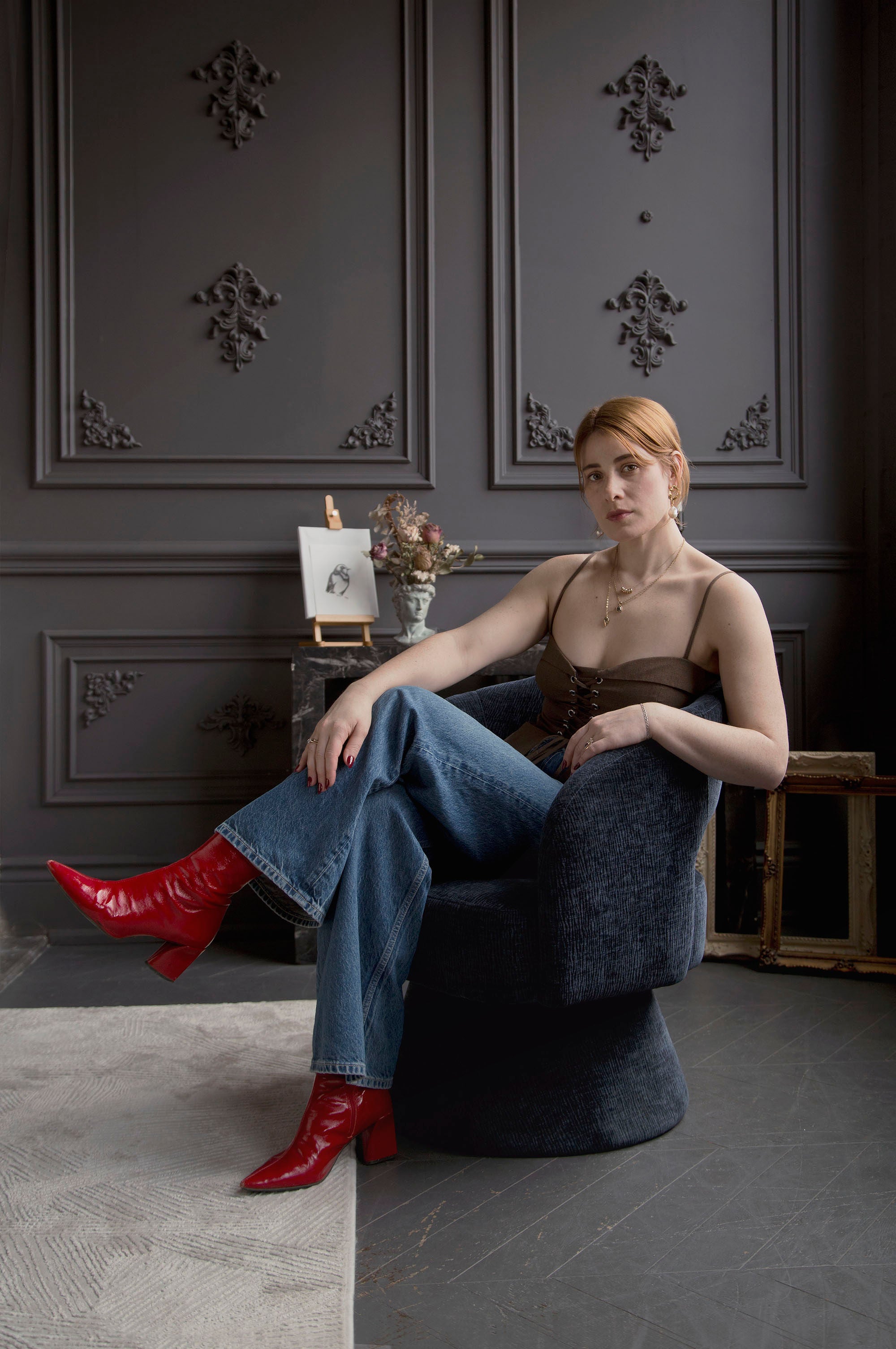Founder of Invidiosa Jewelry, sitting in a chair with bright red boots in an estate living room 